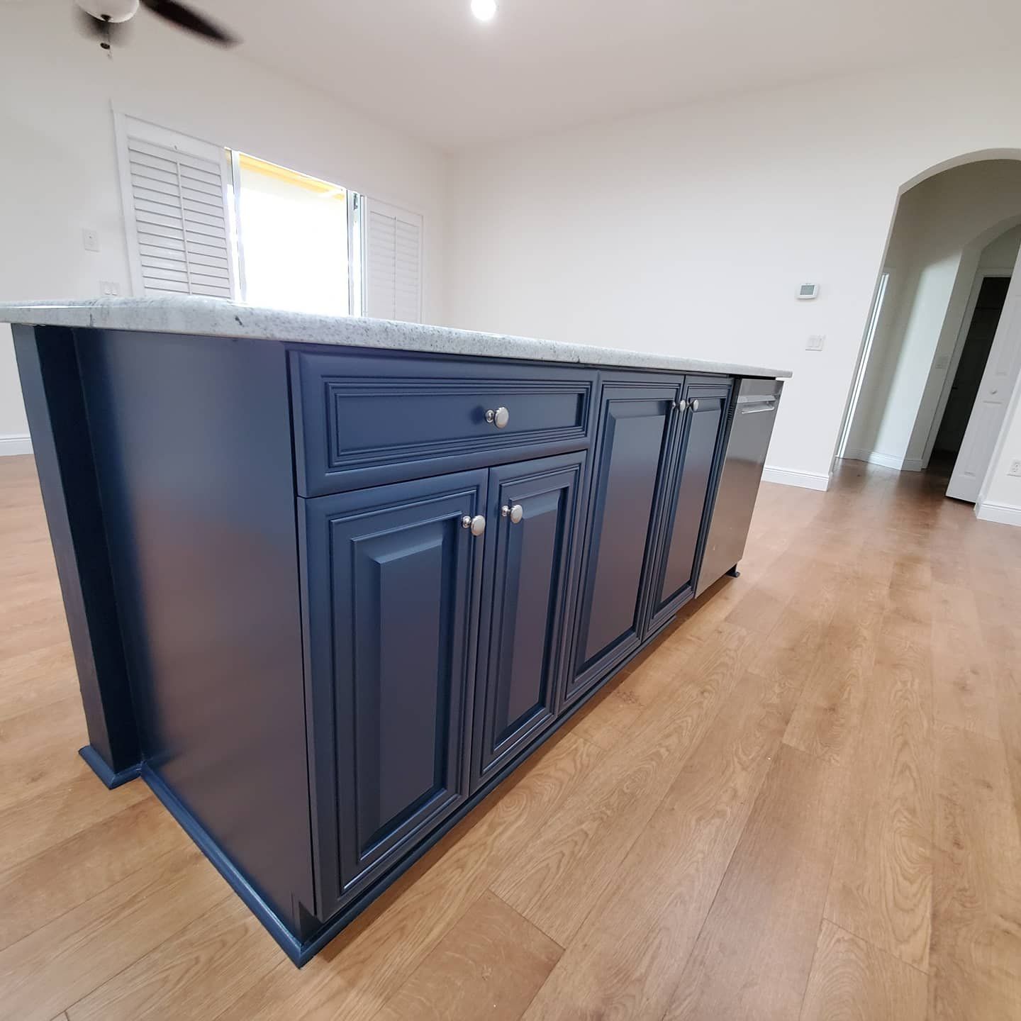 Navy blue kitchen island with a gray countertop in a room with wood floors.