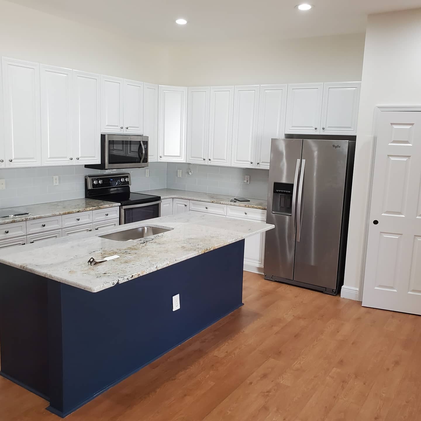 Modern kitchen with white cabinets, blue island, granite countertops, and stainless steel appliances.