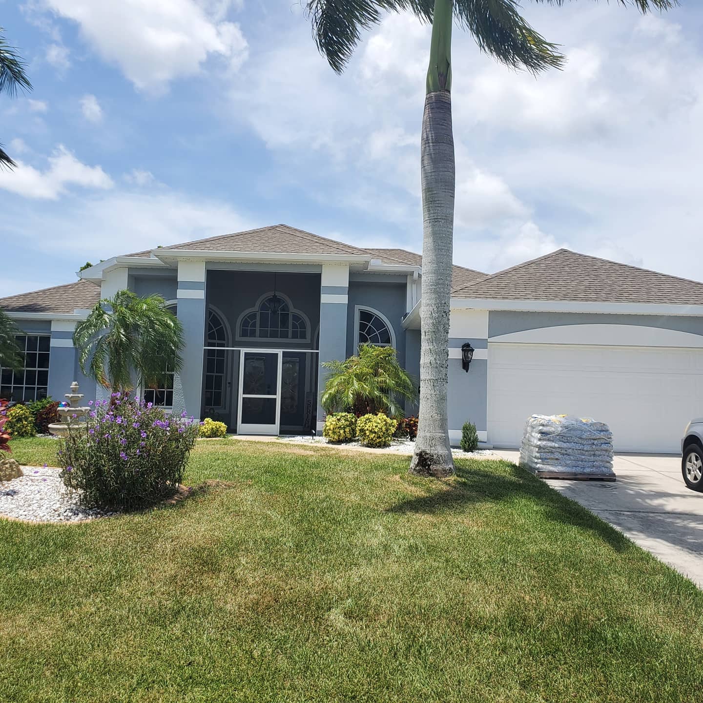 Blue house with white trim, gray roof, palm tree, green lawn, and car parked in driveway.