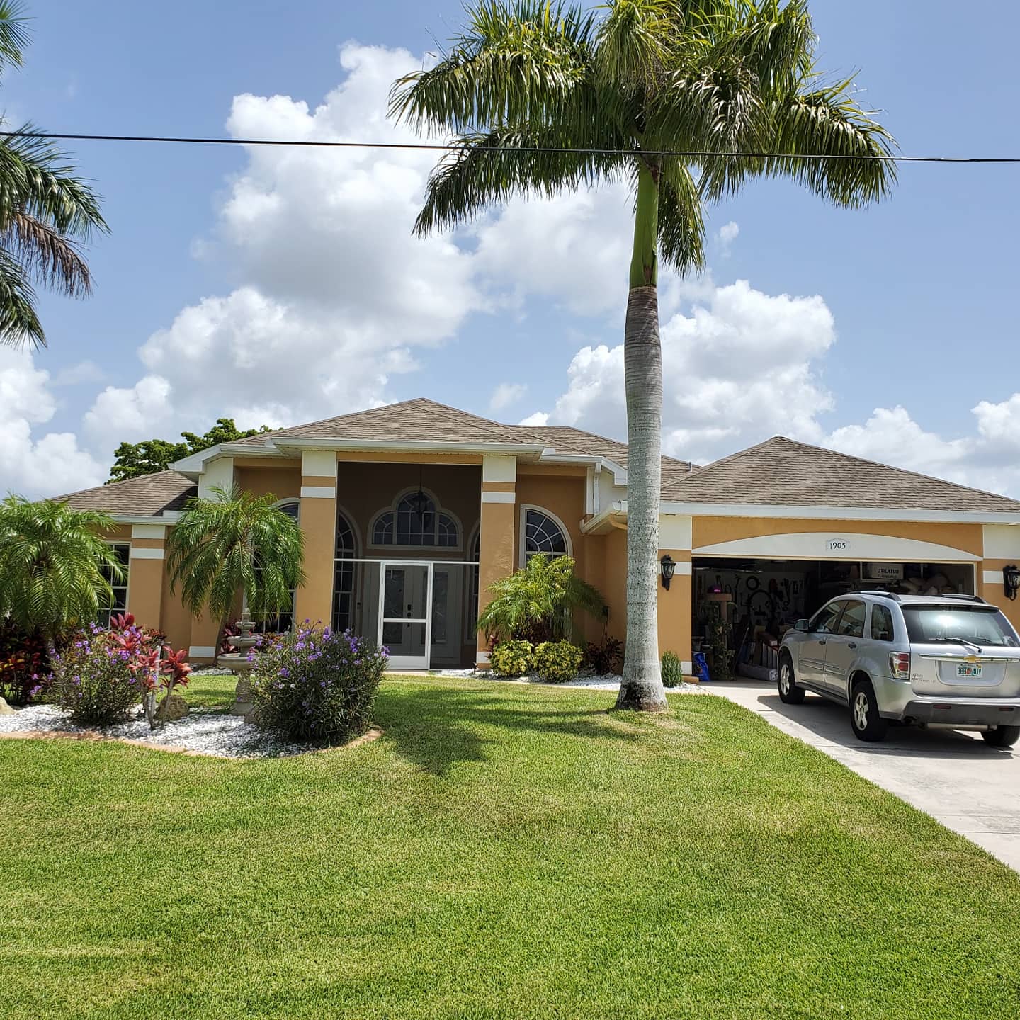 Yellow house with a palm tree, SUV in driveway, and blue sky with clouds.