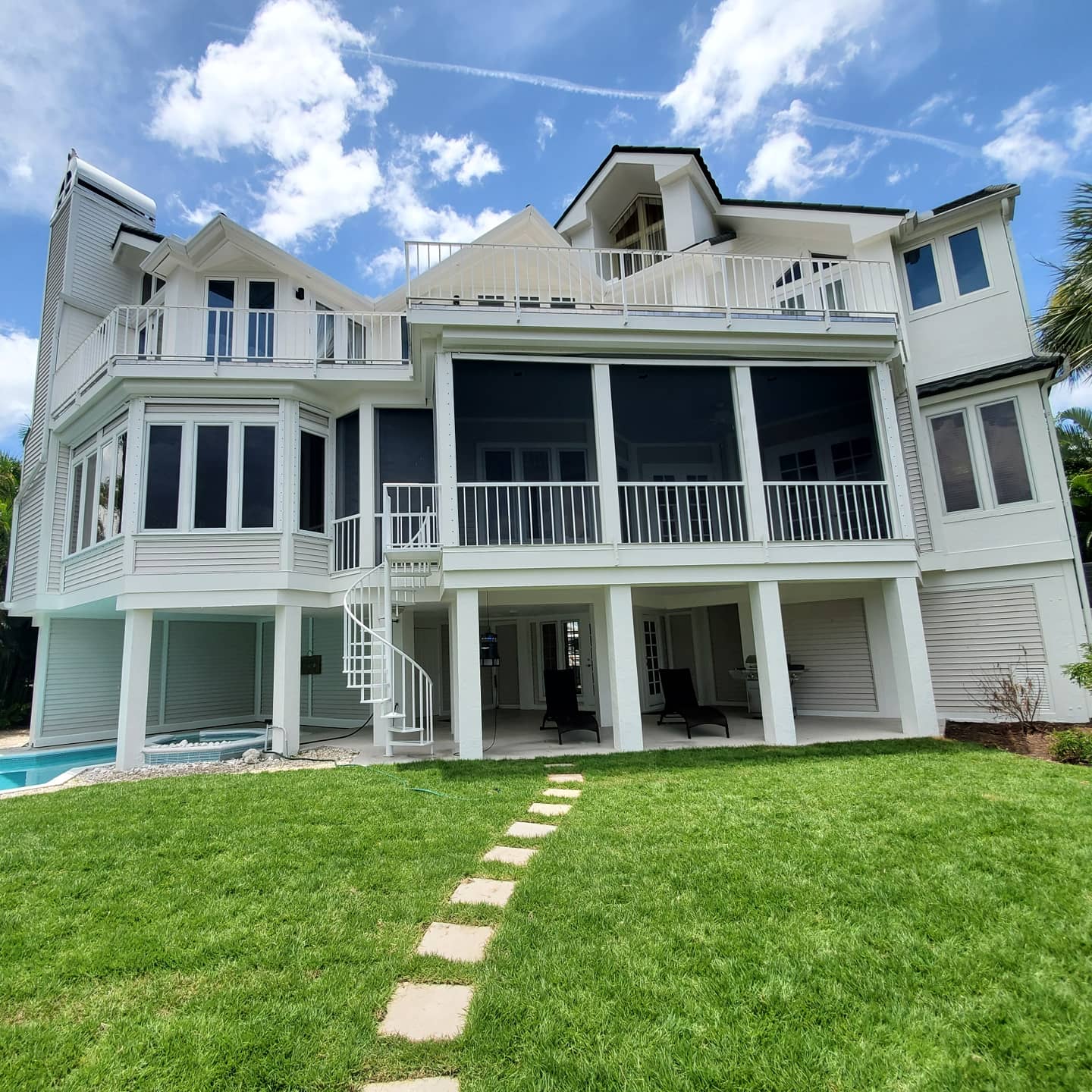White multi-story house with porch, spiral staircase, and green lawn under a blue sky.