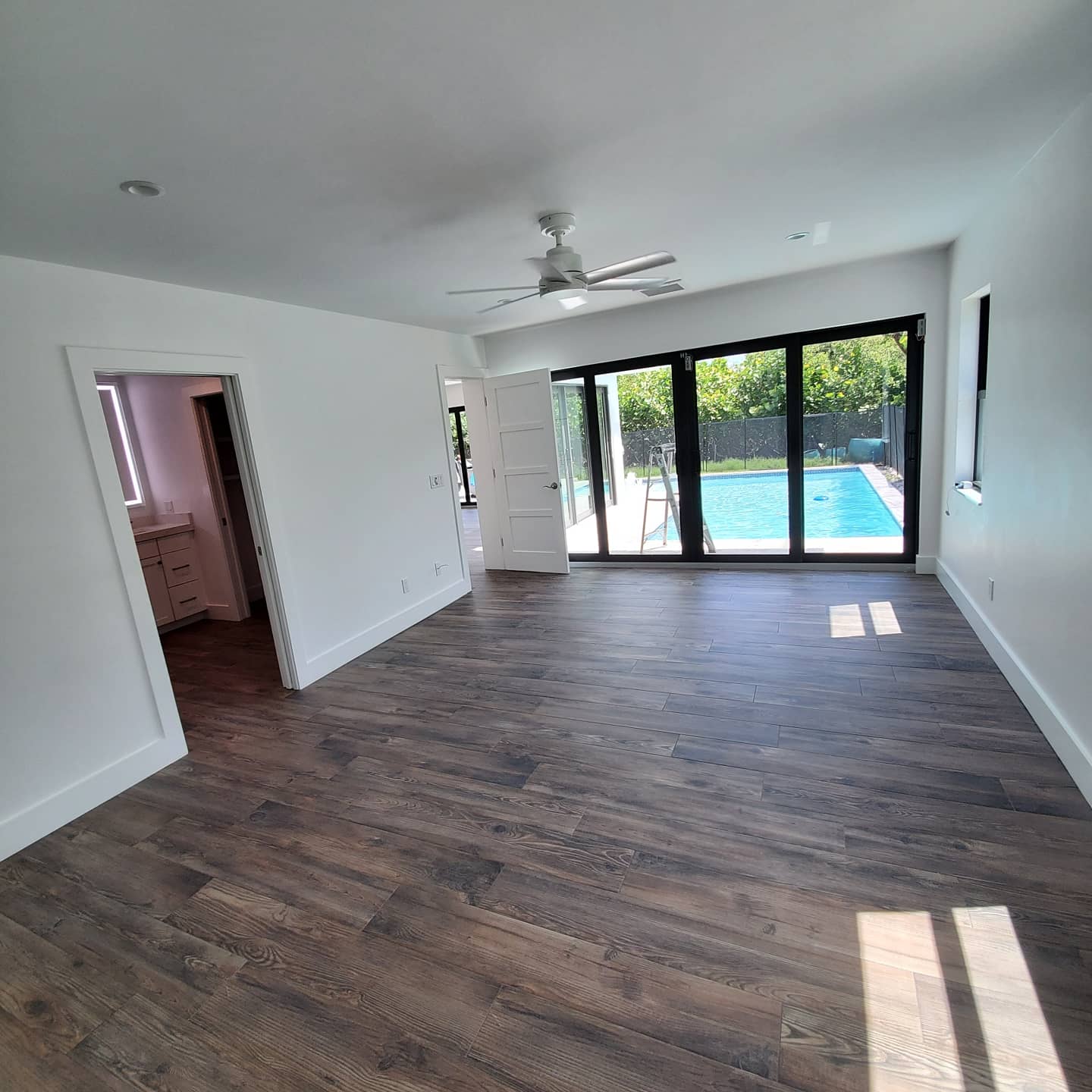 Room with dark wood floors, white walls, and glass doors leading to a pool.