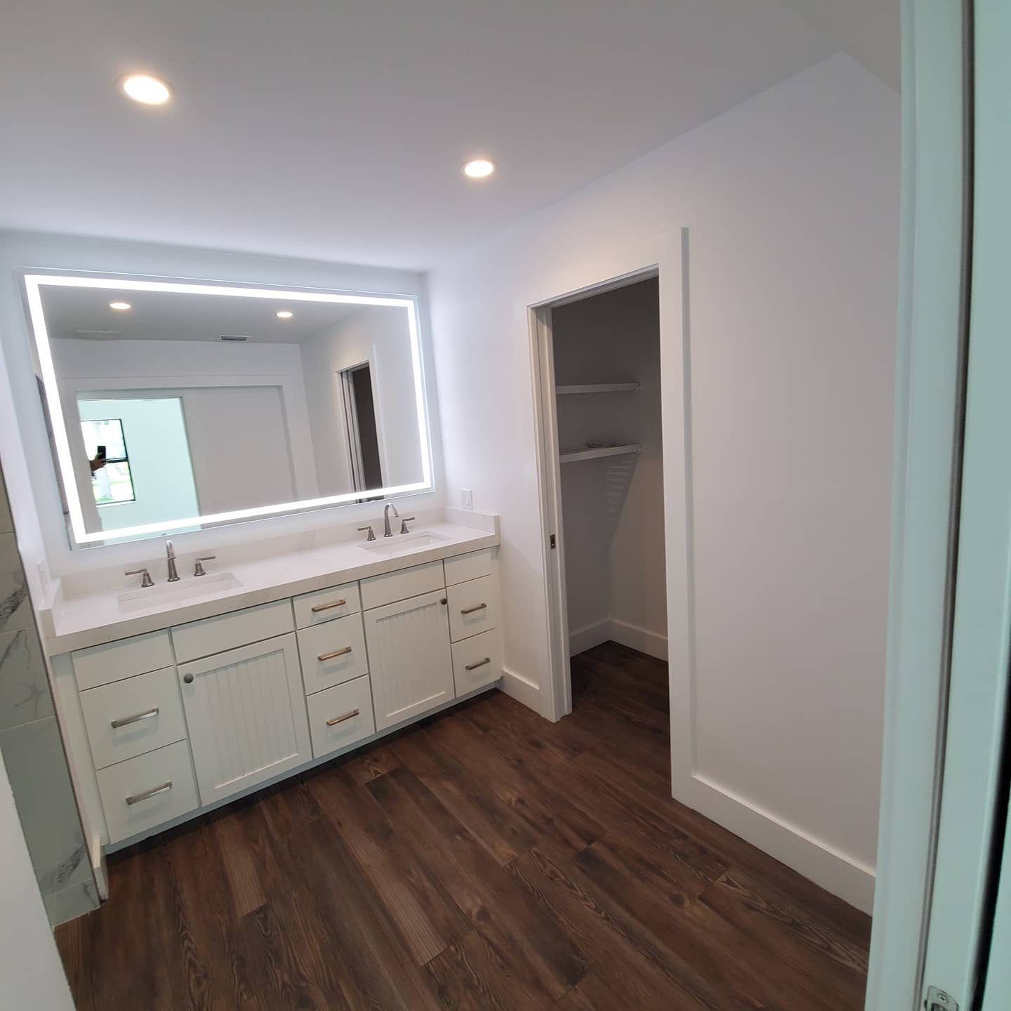 Modern white bathroom with a large mirror and wood flooring.