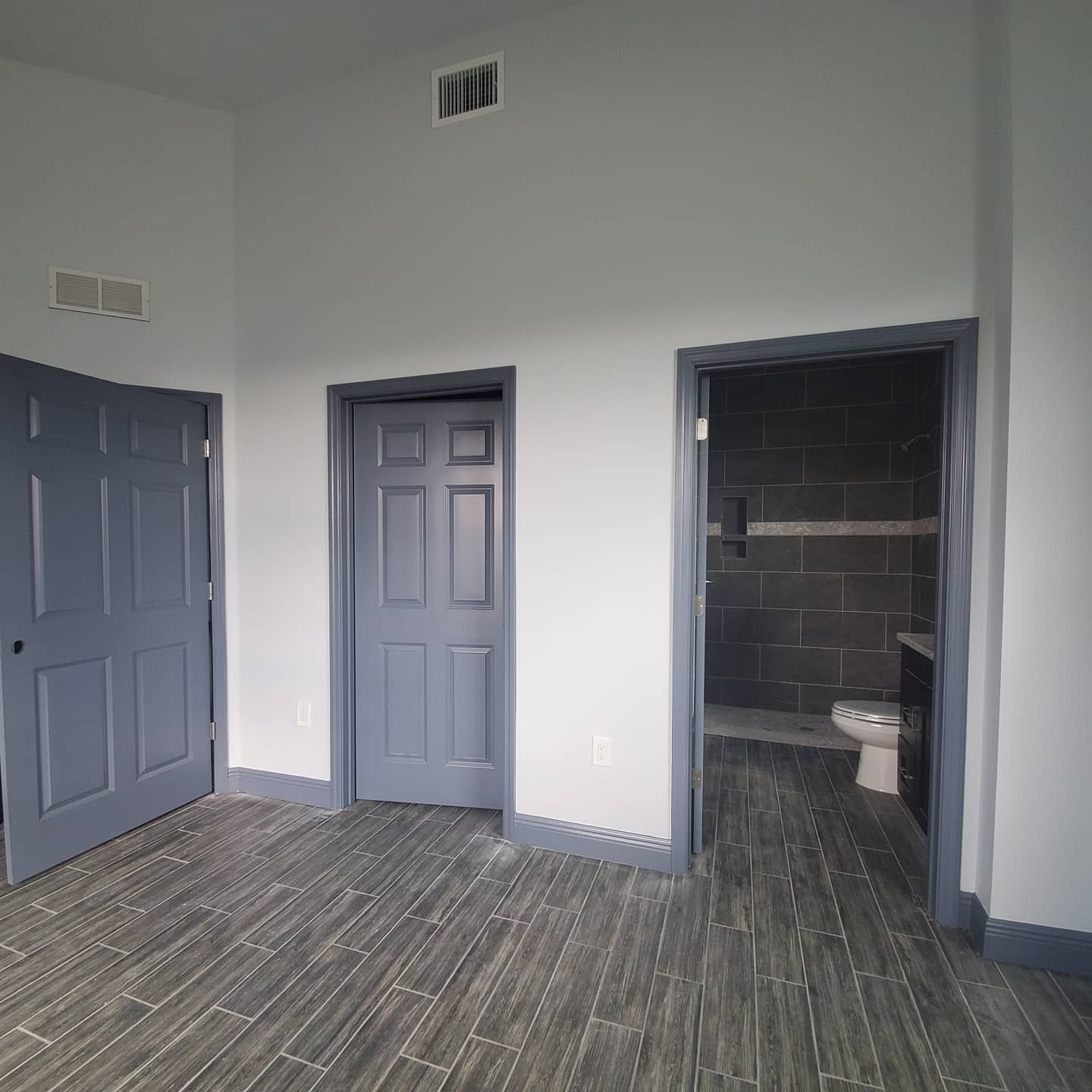 Blue-painted doors in a room with gray flooring and a view of a bathroom with a gray tiled shower.