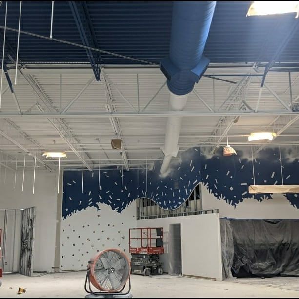 Interior of a building under construction. Blue ceiling, white walls, a large fan, and a lift.