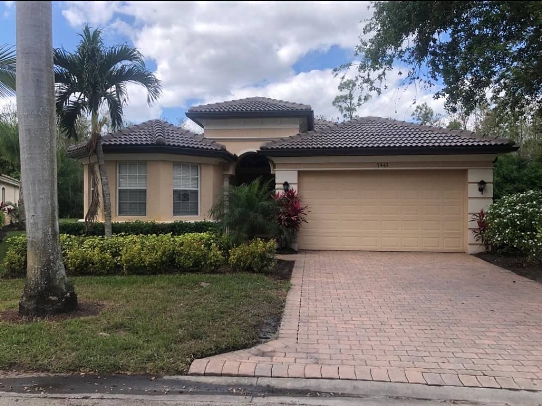 Tan house with brown tile roof, garage, brick driveway, and landscaping.