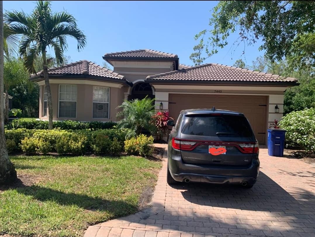 House with a brown tile roof, tan walls, and a parked black SUV in the driveway.
