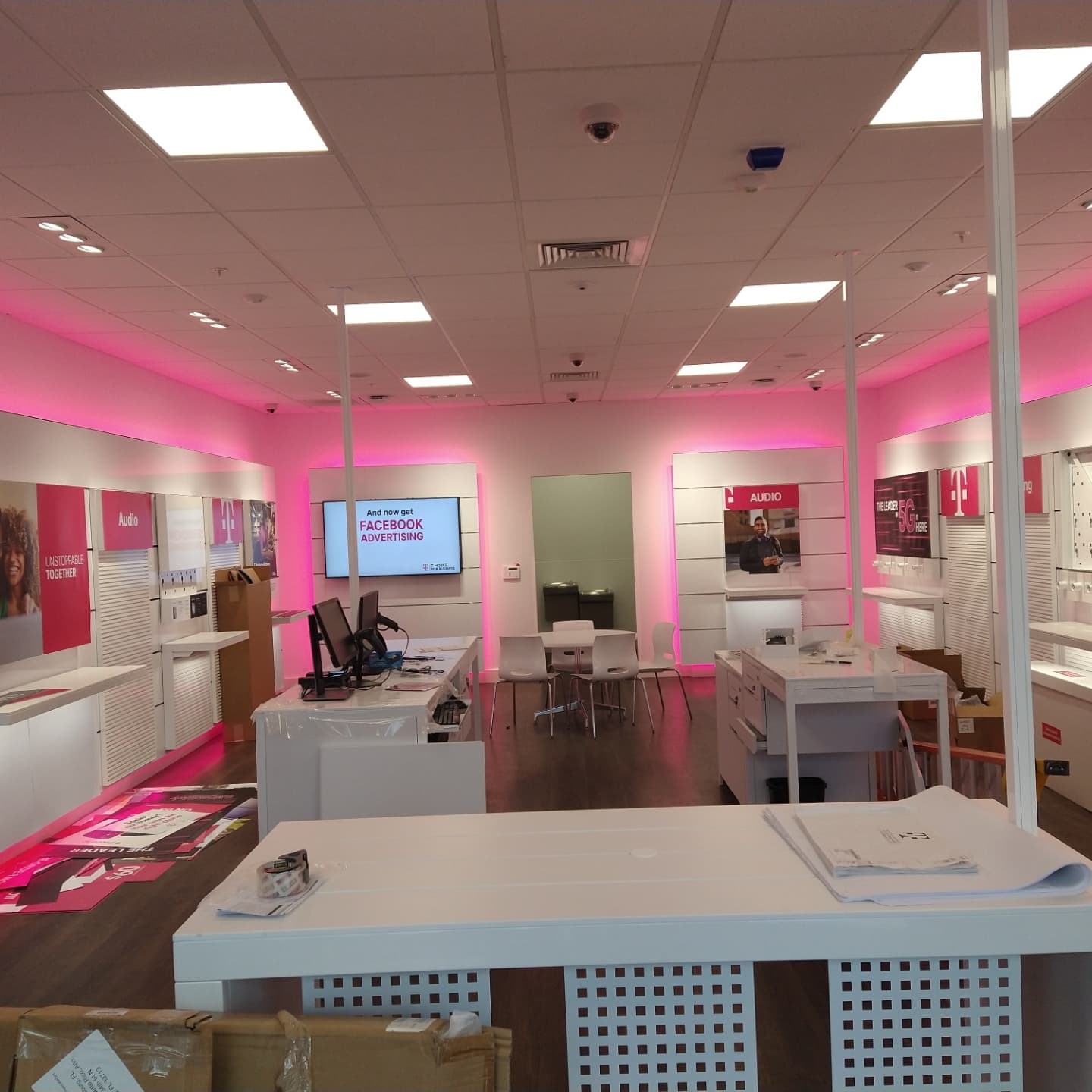 Interior of a T-Mobile store with pink accent lighting, white displays, and a central counter.