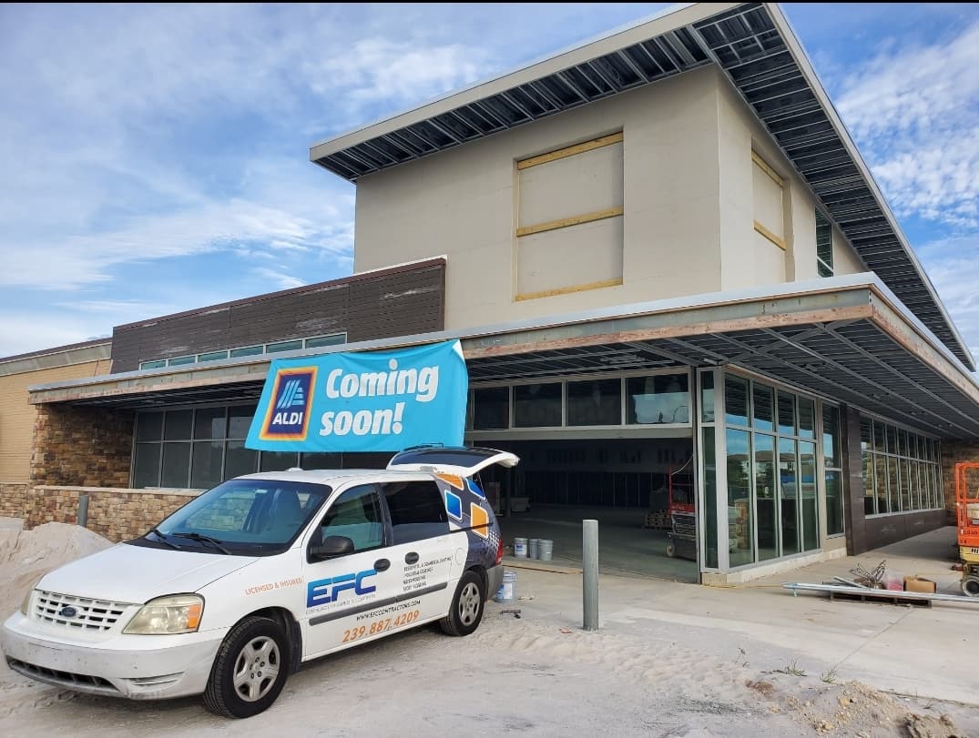 A white Ford work van parked in front of a soon-to-open Aldi grocery store under construction.