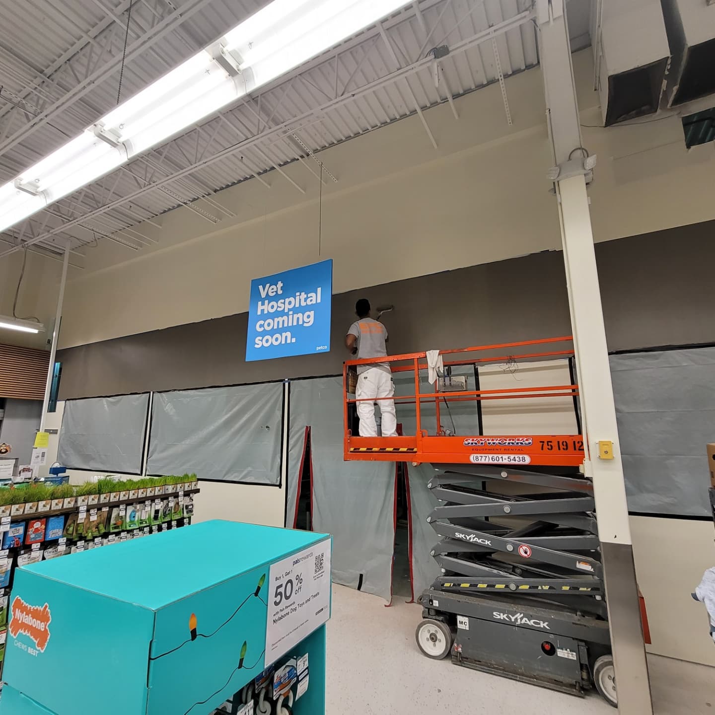 A worker on a lift paints a wall in a store, with a sign reading