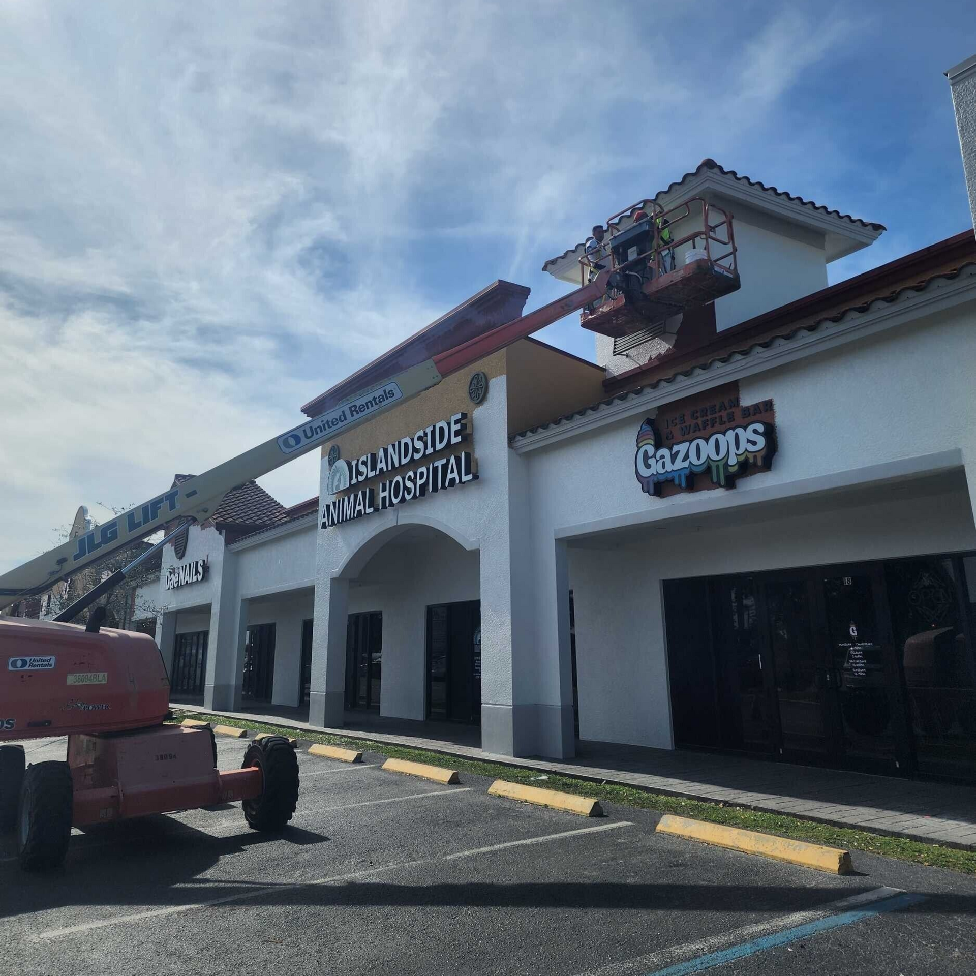 Exterior of a strip mall with a lift servicing a sign that reads