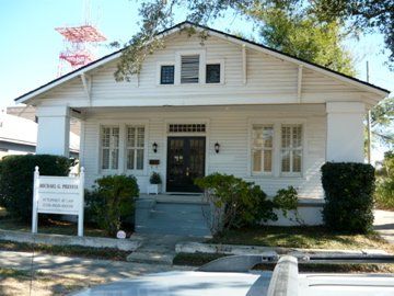 White house with a sign in front; porch, shrubs, and windows visible.