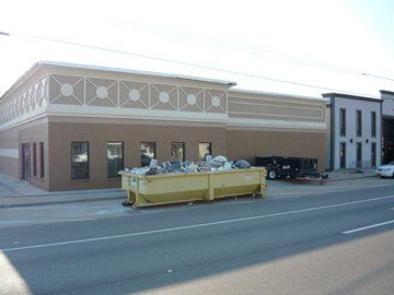 A tan building with a dumpster in front. The building has a decorative top, windows, and is next to a street.