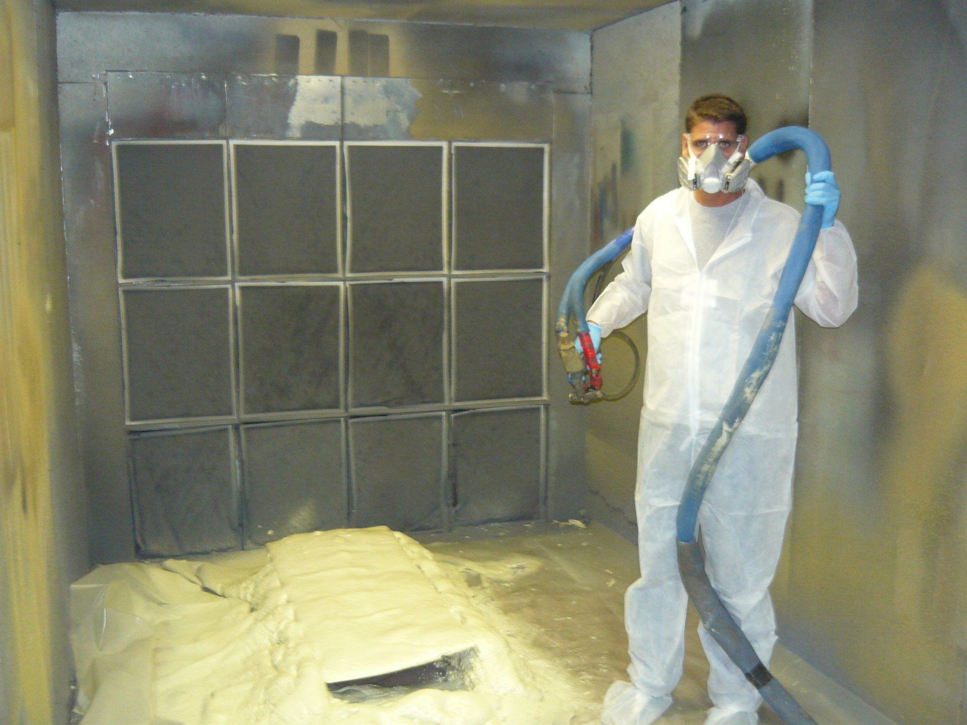 Person in protective suit spraying foam insulation in a small, enclosed room.