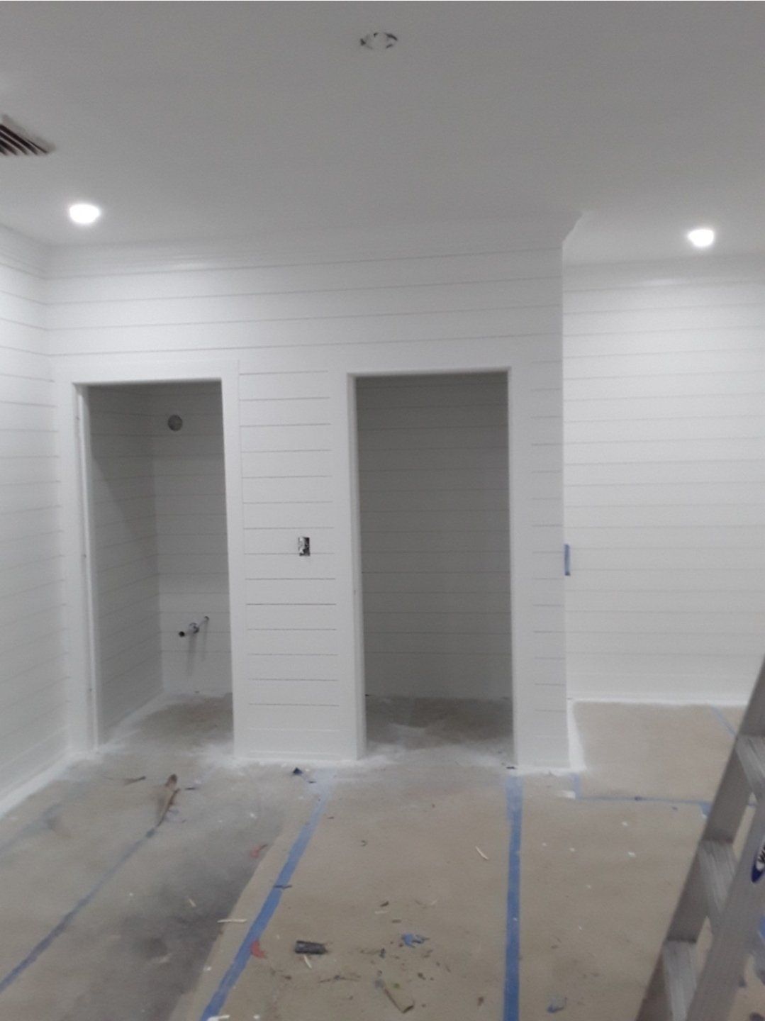 Two white-painted doorways, likely bathrooms, under construction in a room with white horizontal paneling on the walls and concrete floor.