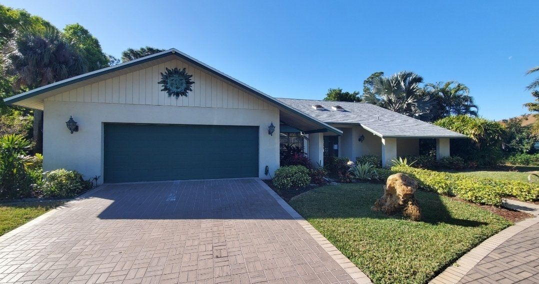 Beige house with teal garage door and trim, gray roof, sunny day.