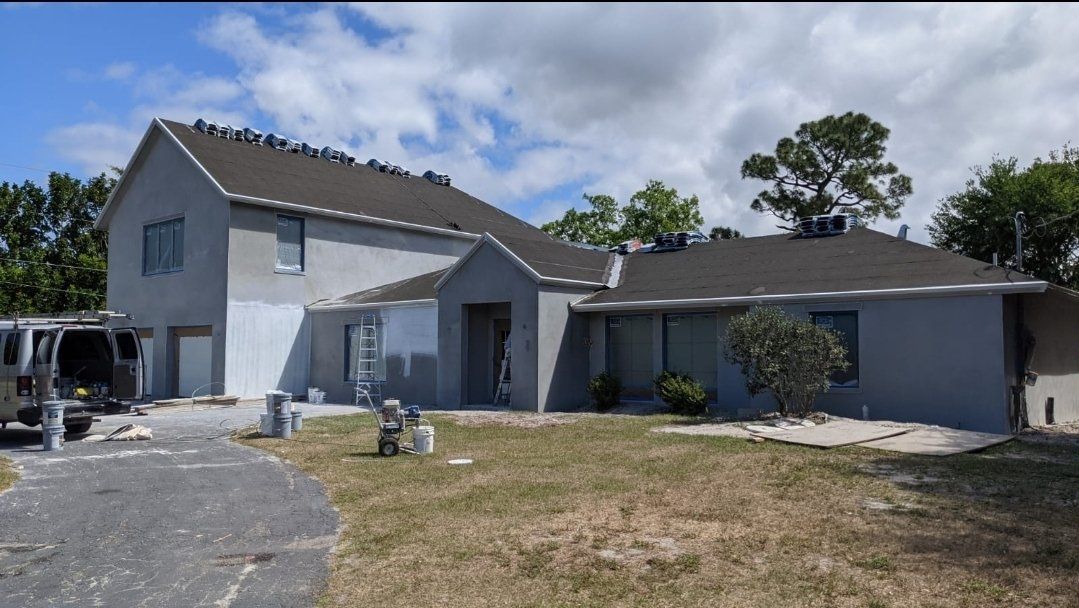 Gray stucco house undergoing roof replacement, parked van in the drive, cloudy sky.