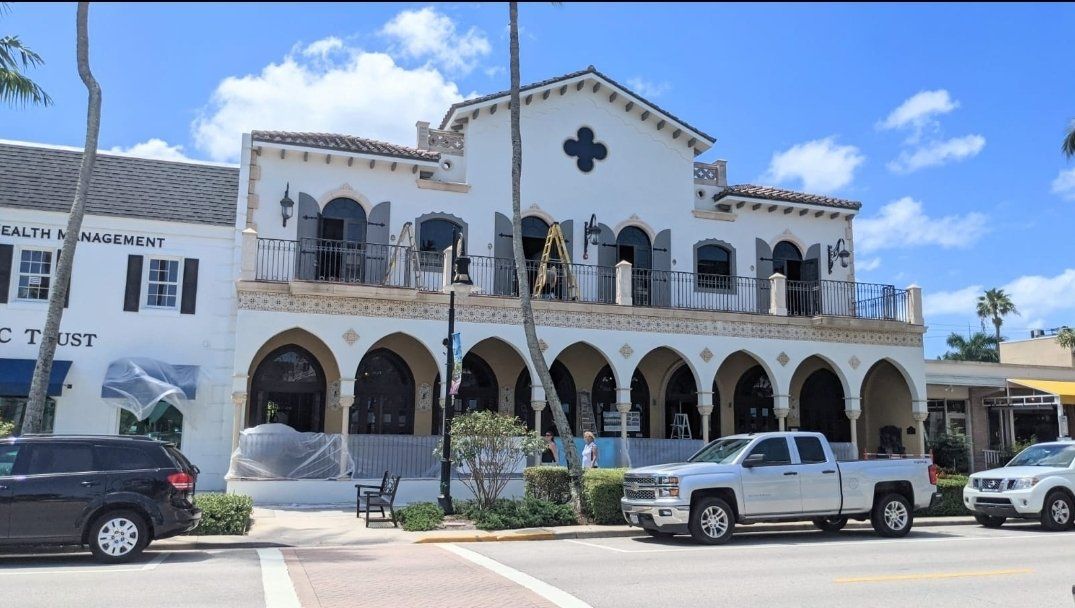 White Mediterranean-style building with arched windows and balconies; cars parked on street.