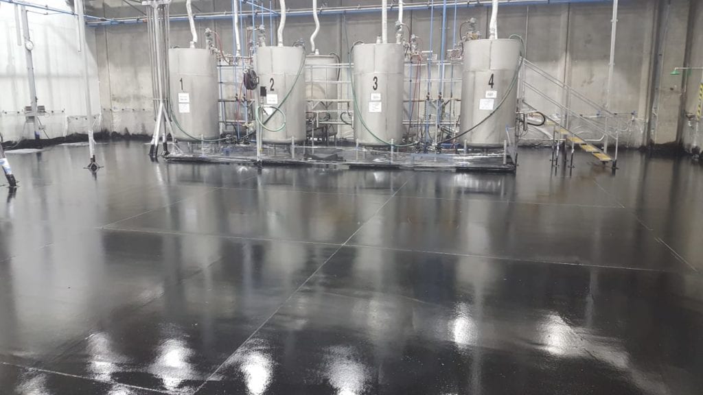 Shiny black industrial floor with metallic tanks and pipes.