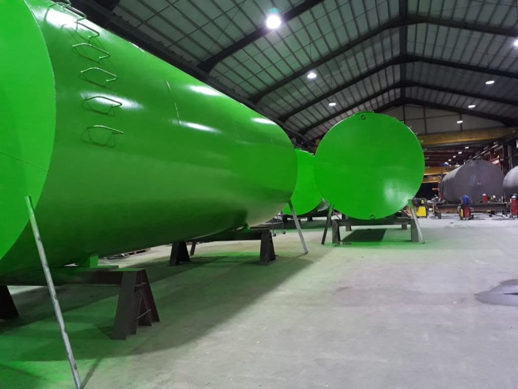 Green industrial tanks in a workshop, lit by overhead lights.