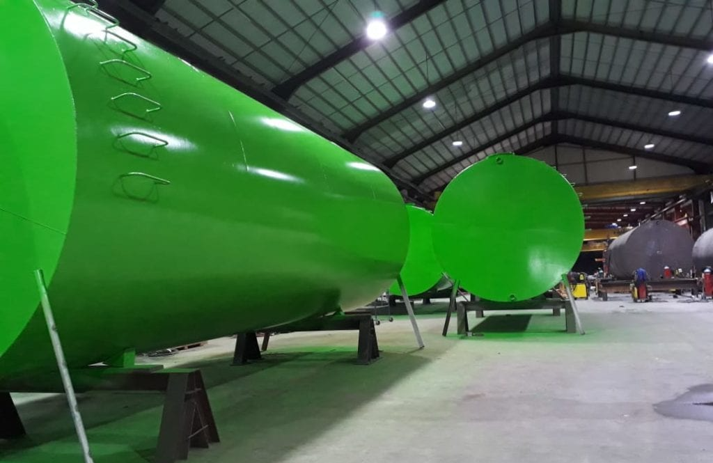 Large green industrial tanks in a warehouse, supported by stands.