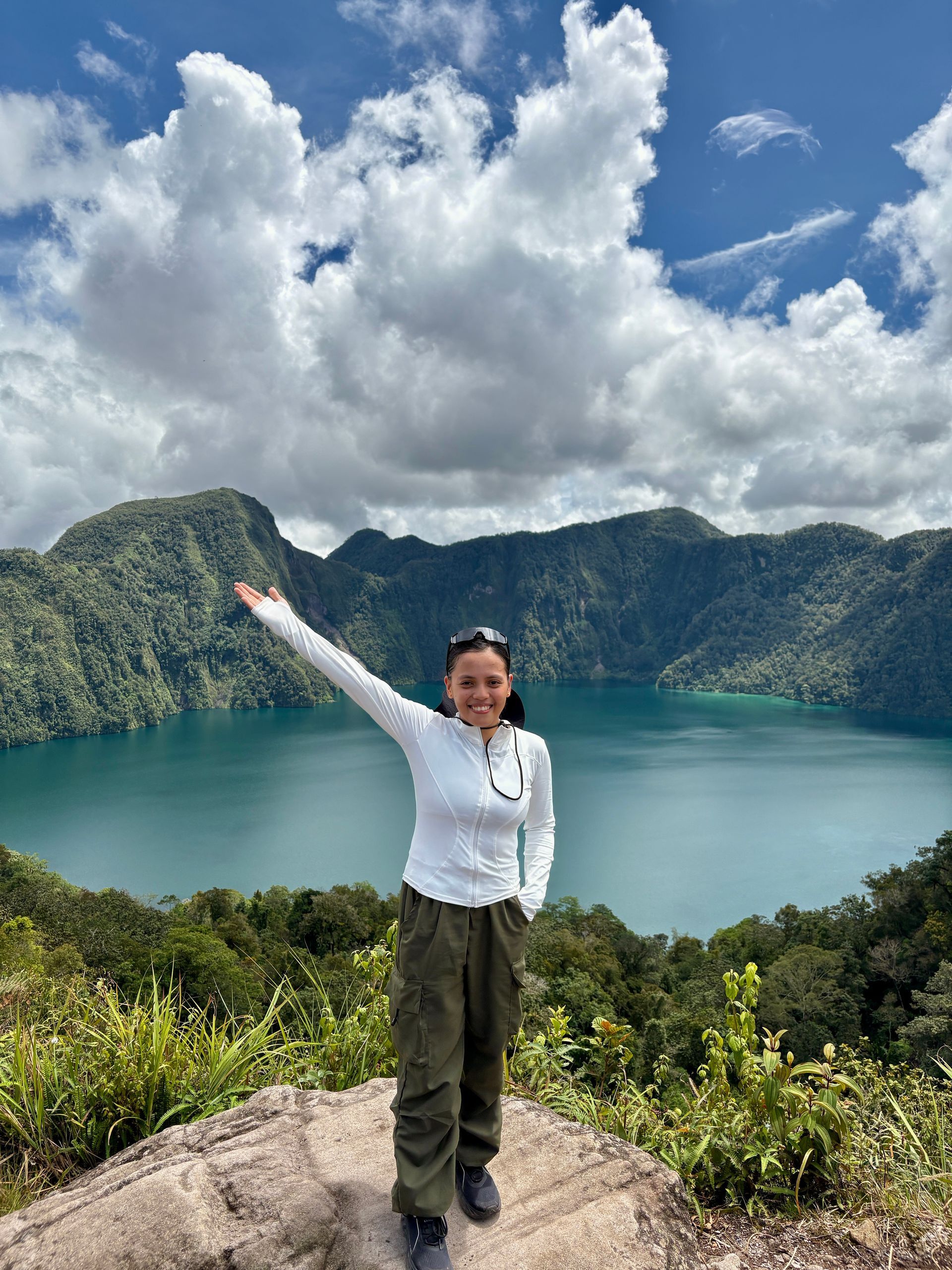 Angel, Motorcycle Sponsorship Program Manager at Avenir Consulting, pointing proudly at mountain lake view.