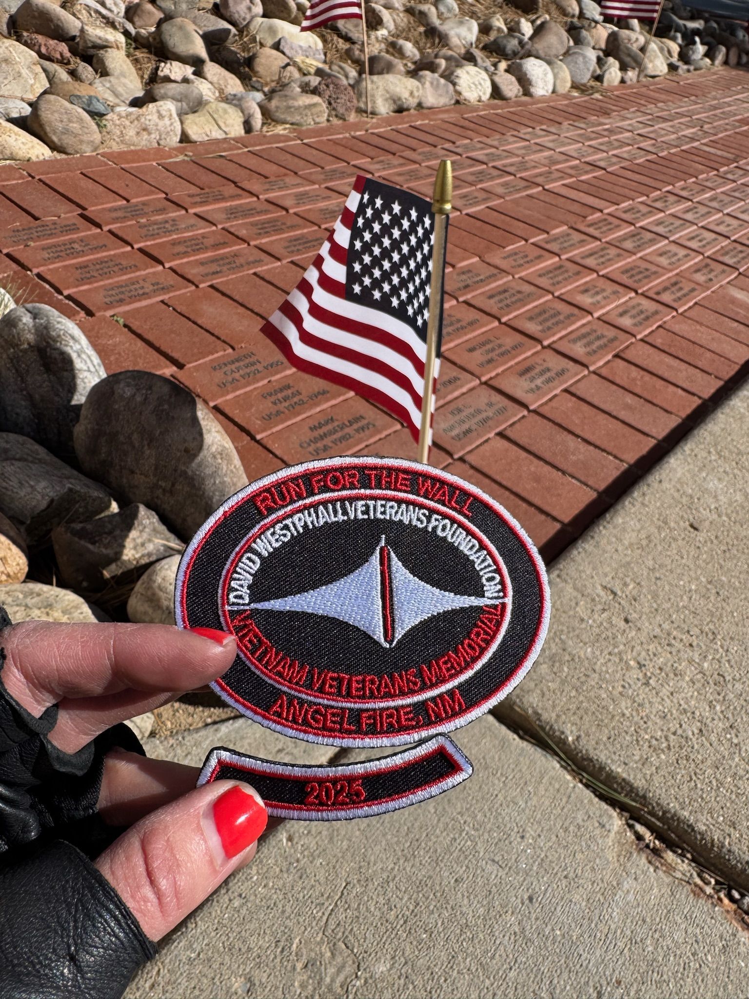 A person is holding a patch with a small american flag in the background.