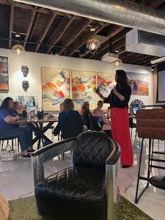 Woman presenting in an art gallery café with abstract paintings and seated patrons.