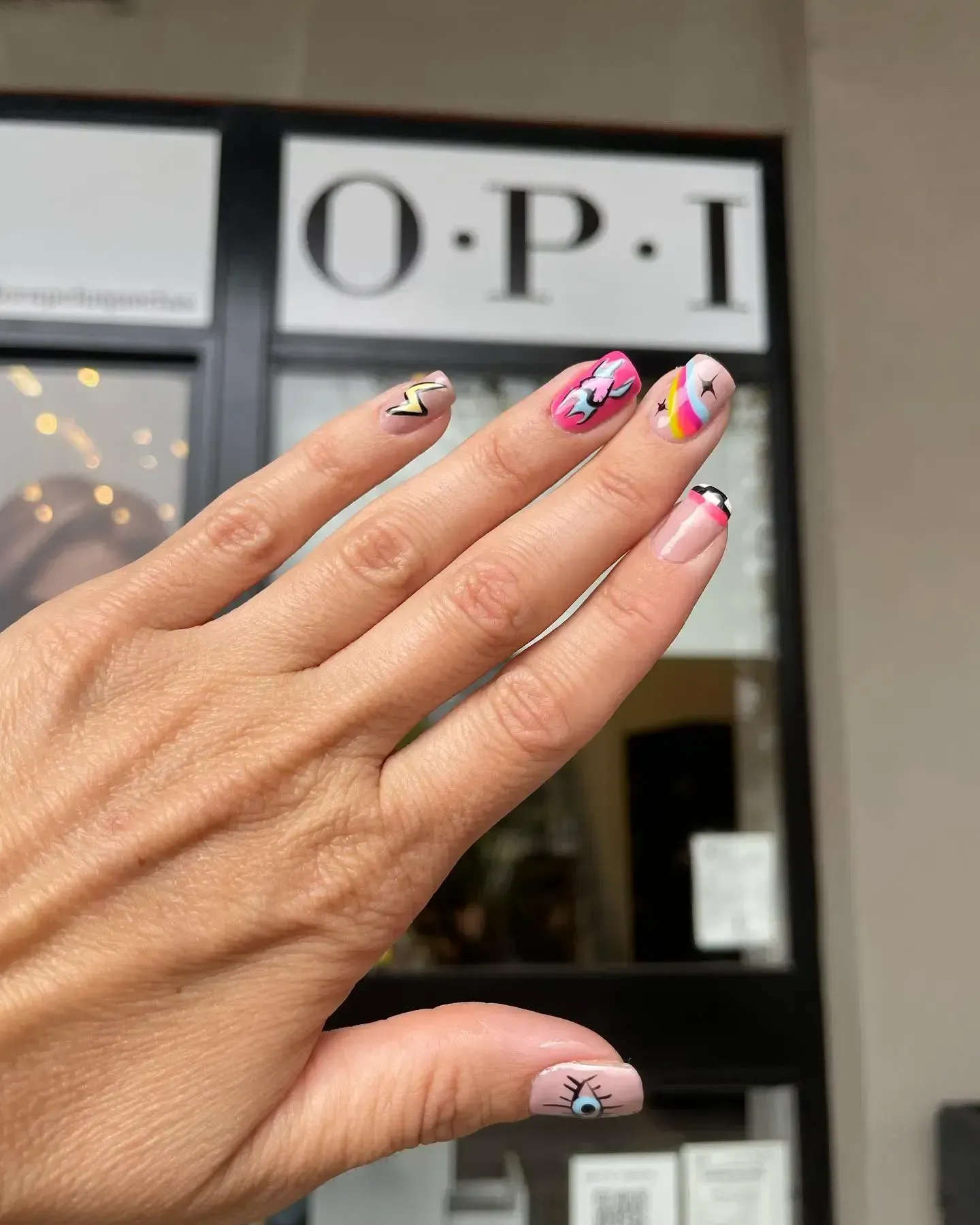 Mano con uñas decoradas en rosa y blanco frente al letrero del salón OPI.