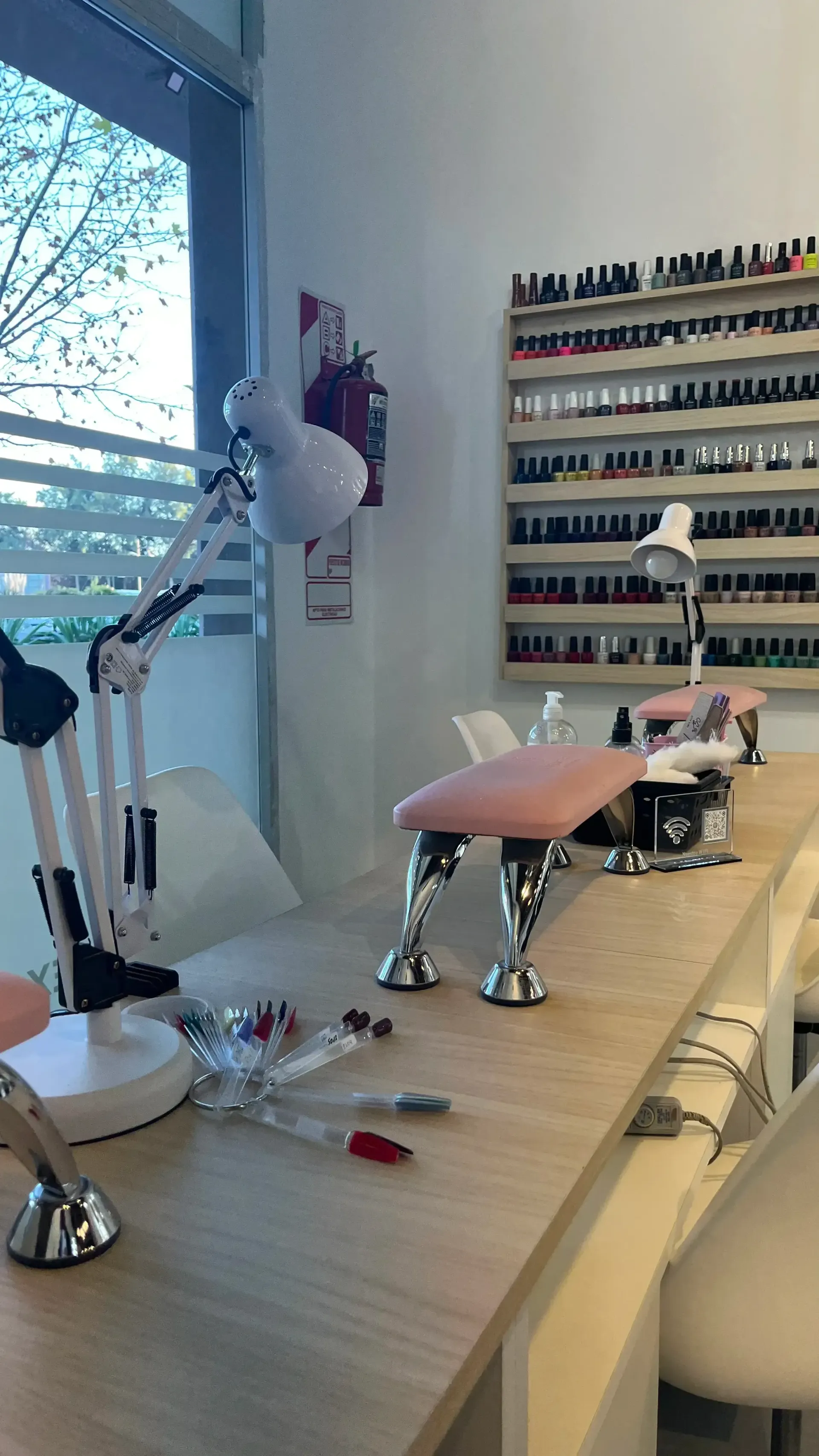 Mesa de manicura con estantes para esmaltes de uñas, lámpara y silla en un luminoso espacio de trabajo de salón de belleza.