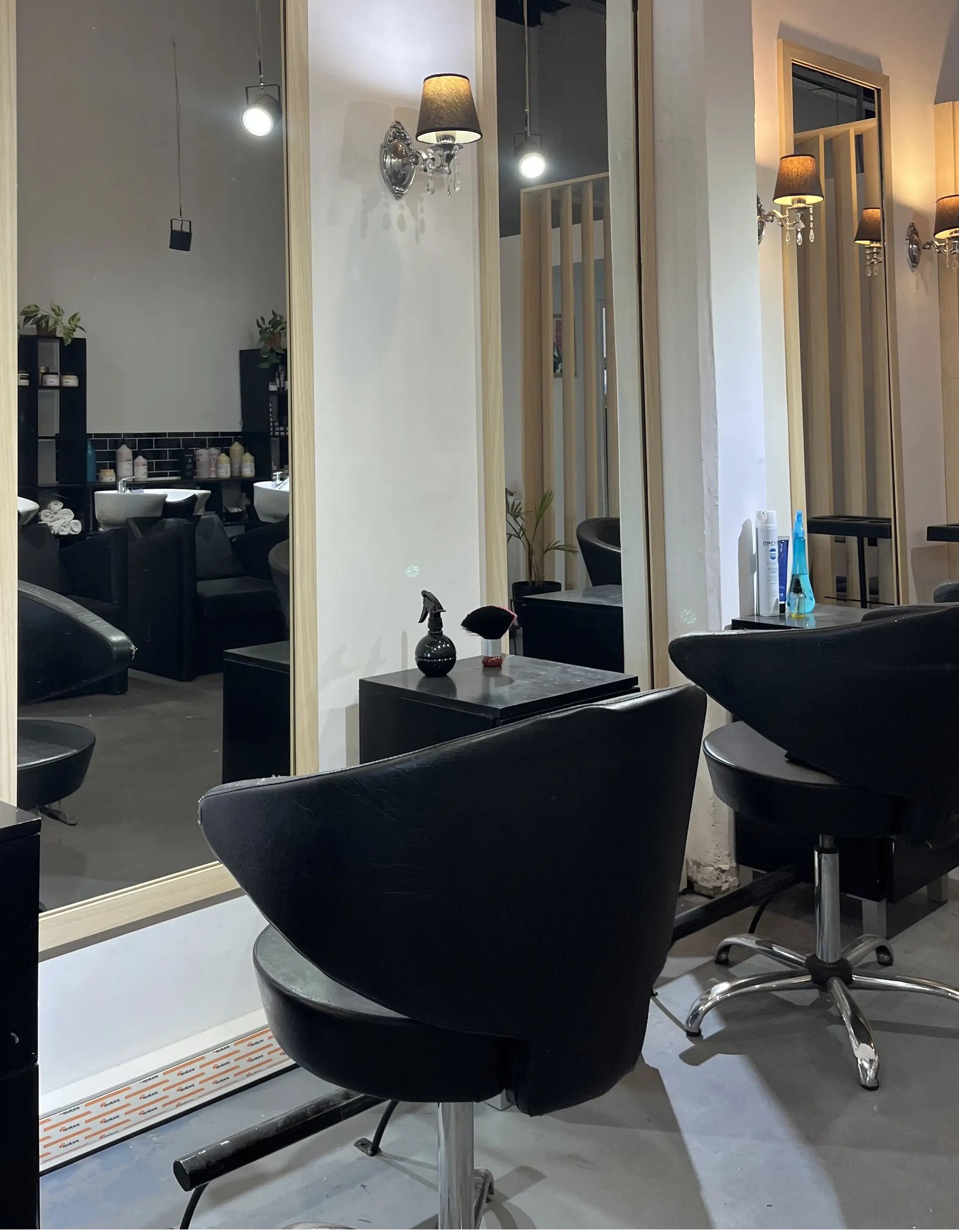 Salón de belleza vacío con sillones de peluquería negros, espejos grandes y apliques de pared brillantes.
