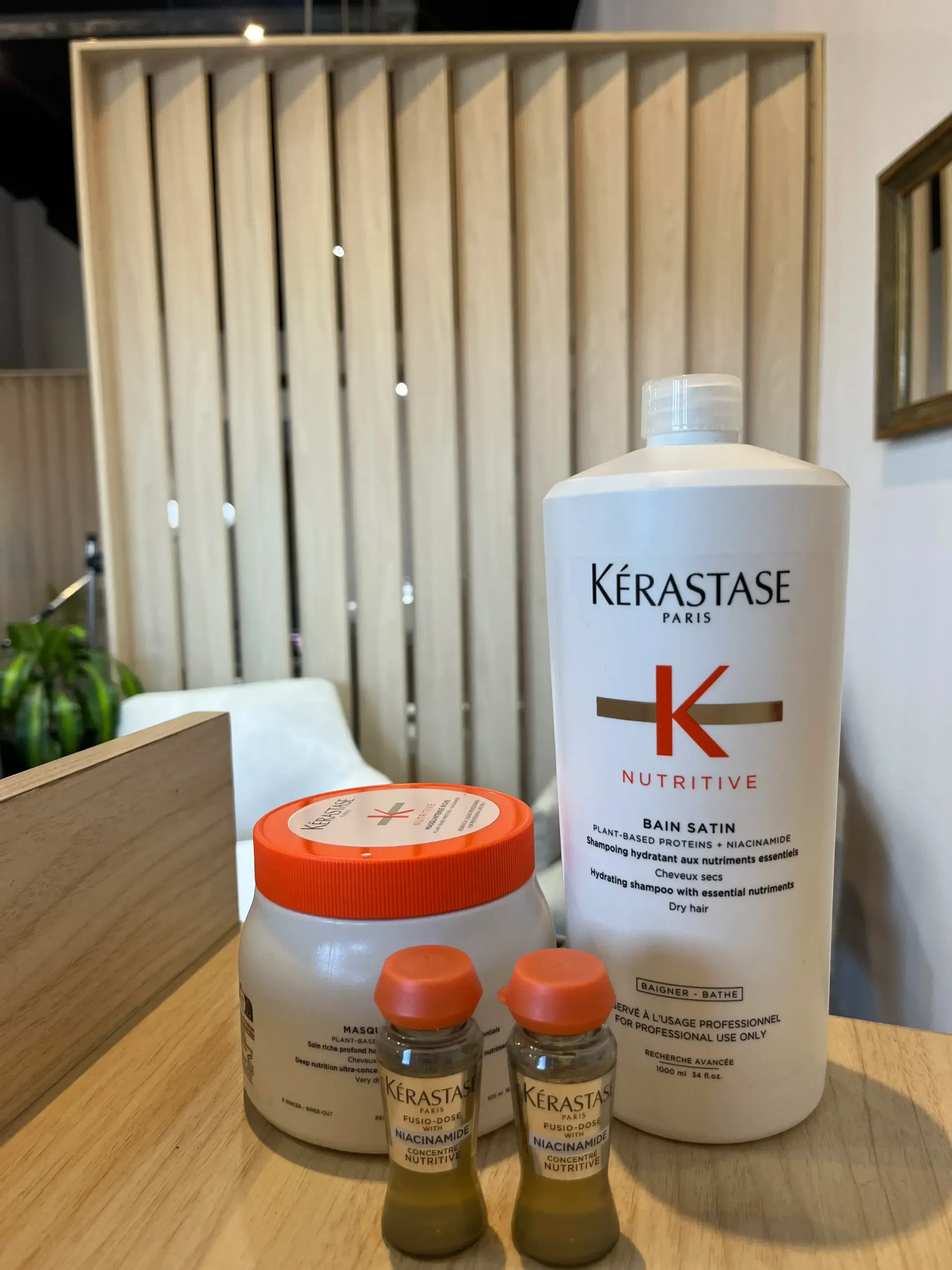 Productos para el cabello Kérastase sobre un mostrador de madera en un ambiente similar al de un salón de belleza.