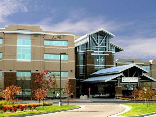 Modern hospital building with glass entrance, tan facade, and landscaped flower beds