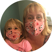 Two people wearing pink face masks, posing closely together indoors.