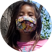 Person wearing a floral face mask outdoors against a blue sky and tree branches