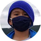 Person wearing a blue knit hat and black face mask outdoors with mountains in the background