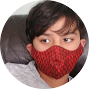 Person wearing a red patterned face mask and gray shirt, looking sideways while seated in a dark chair