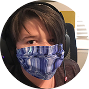 Person wearing a blue patterned face covering and black headphones, looking at the camera indoors.