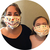 Two people wearing patterned face masks with “health” written on them, seated against a plain wall.