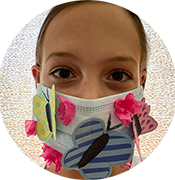 Child wearing a decorated face mask with colorful butterfly and flower cutouts against a textured background