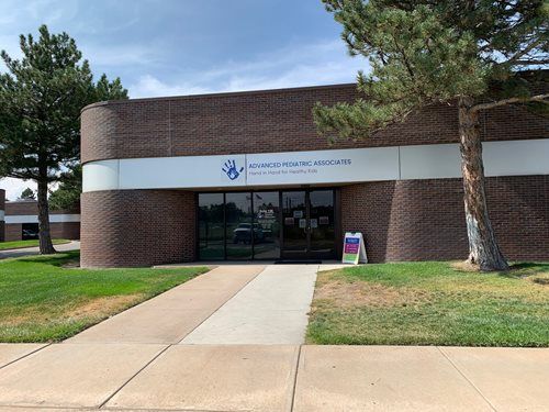 Brick building entrance with glass doors, white sign, and a concrete walkway in front