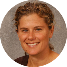 Smiling person with curly hair against a gray background