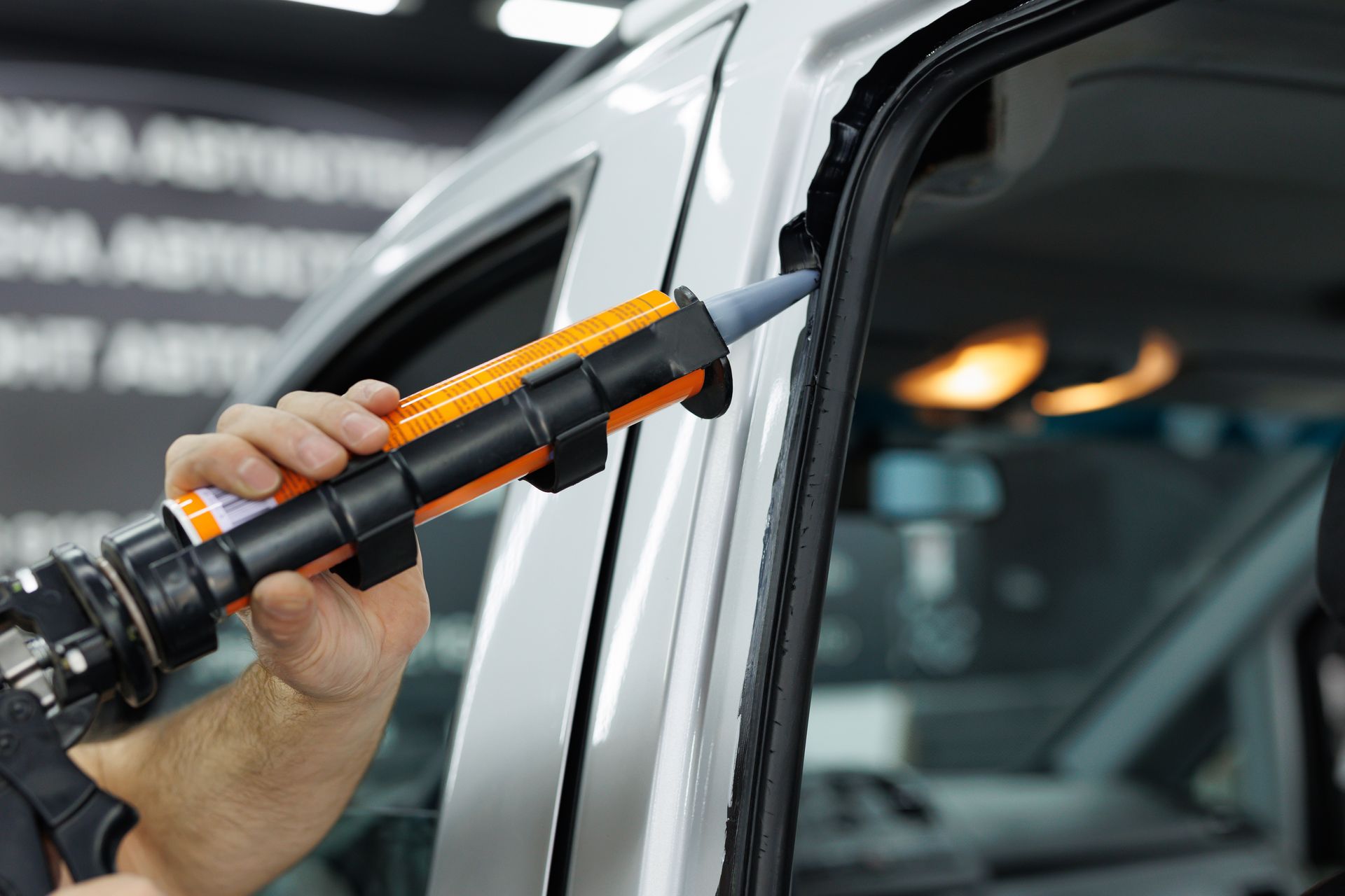 Hand using an orange-and-black tool on a car door seam, likely applying sealant or adhesive