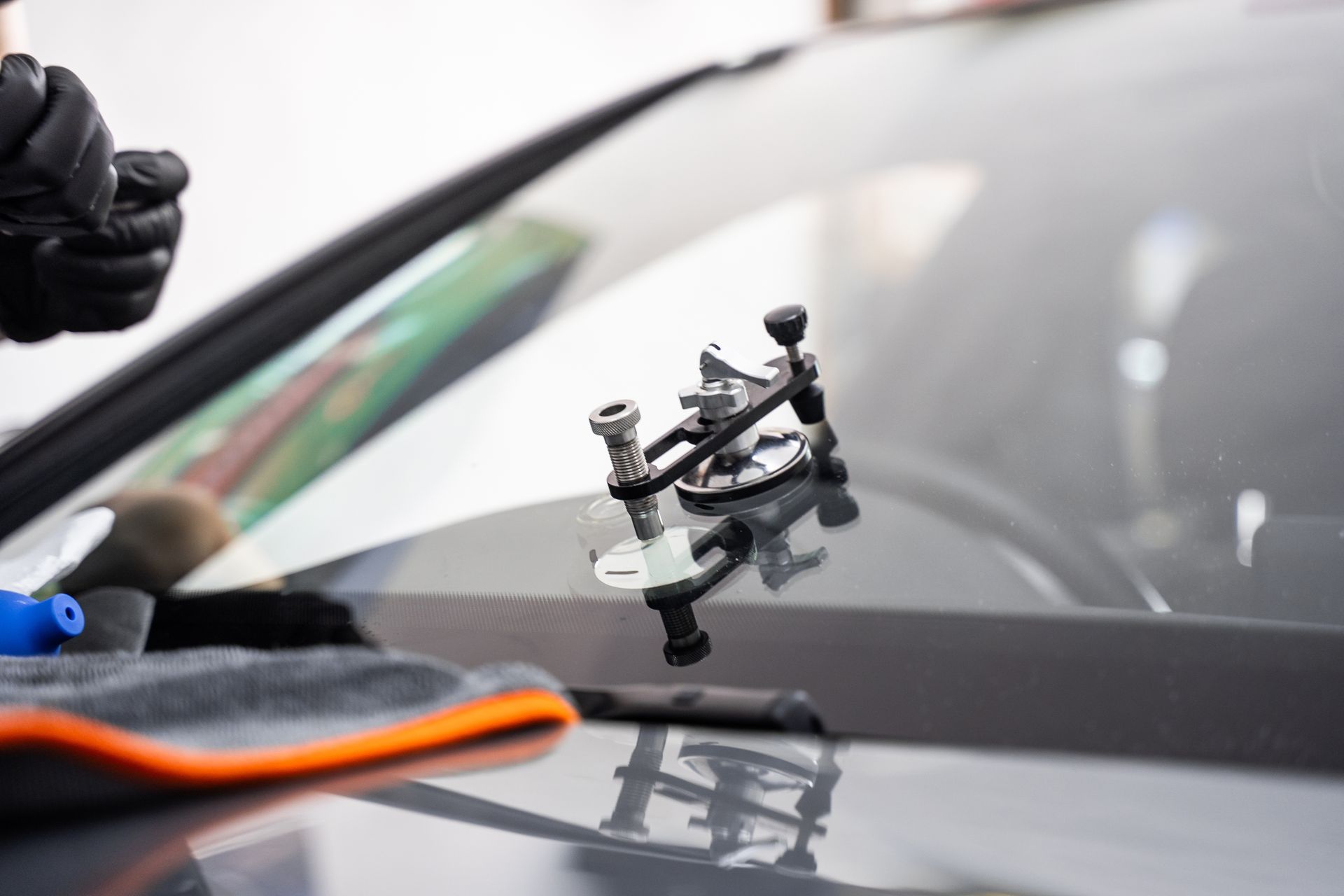 Close-up of a car windshield being repaired with a suction-cup tool and technician’s glove visible