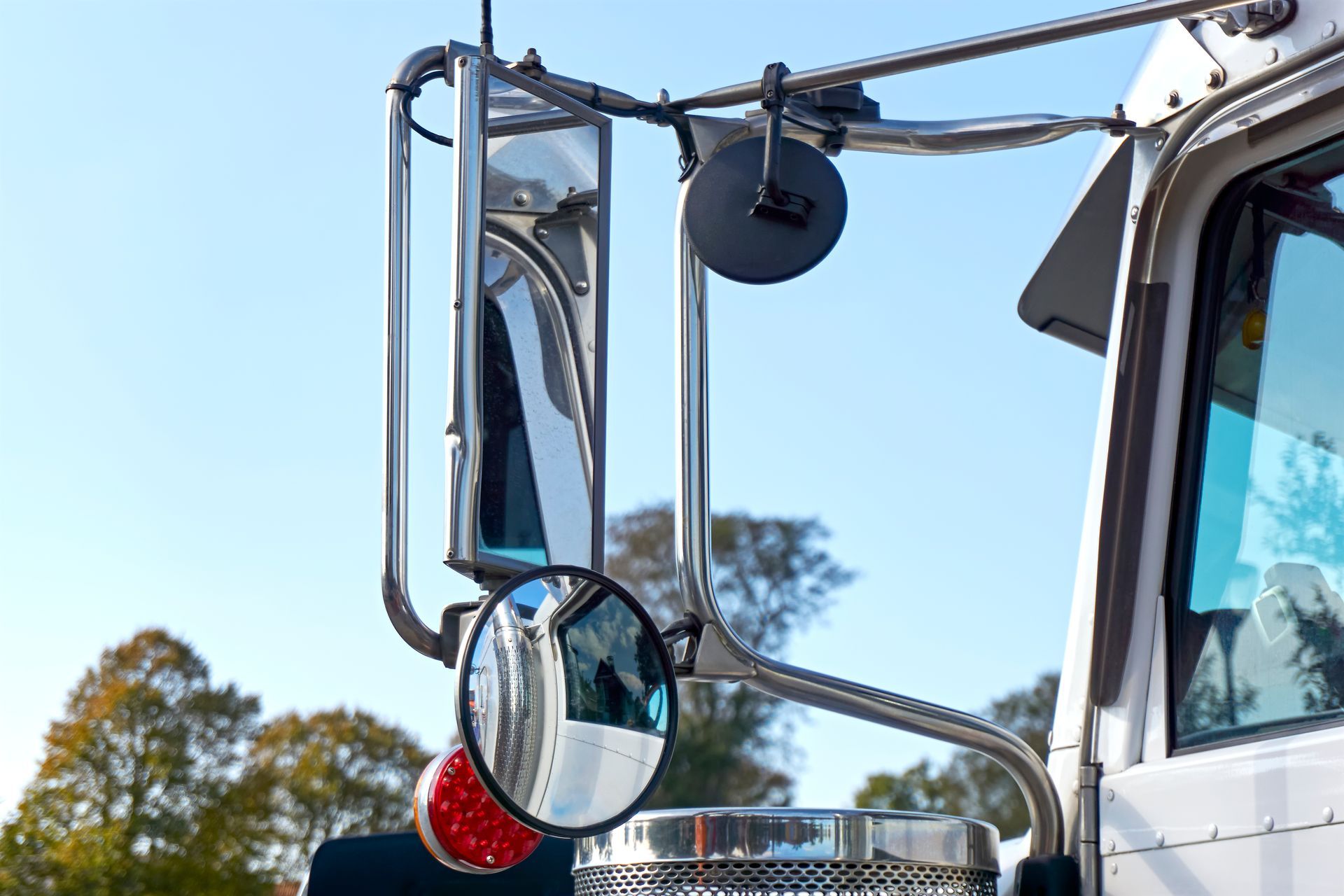 Truck side mirror and chrome frame against a blue sky, with a red reflector visible.
