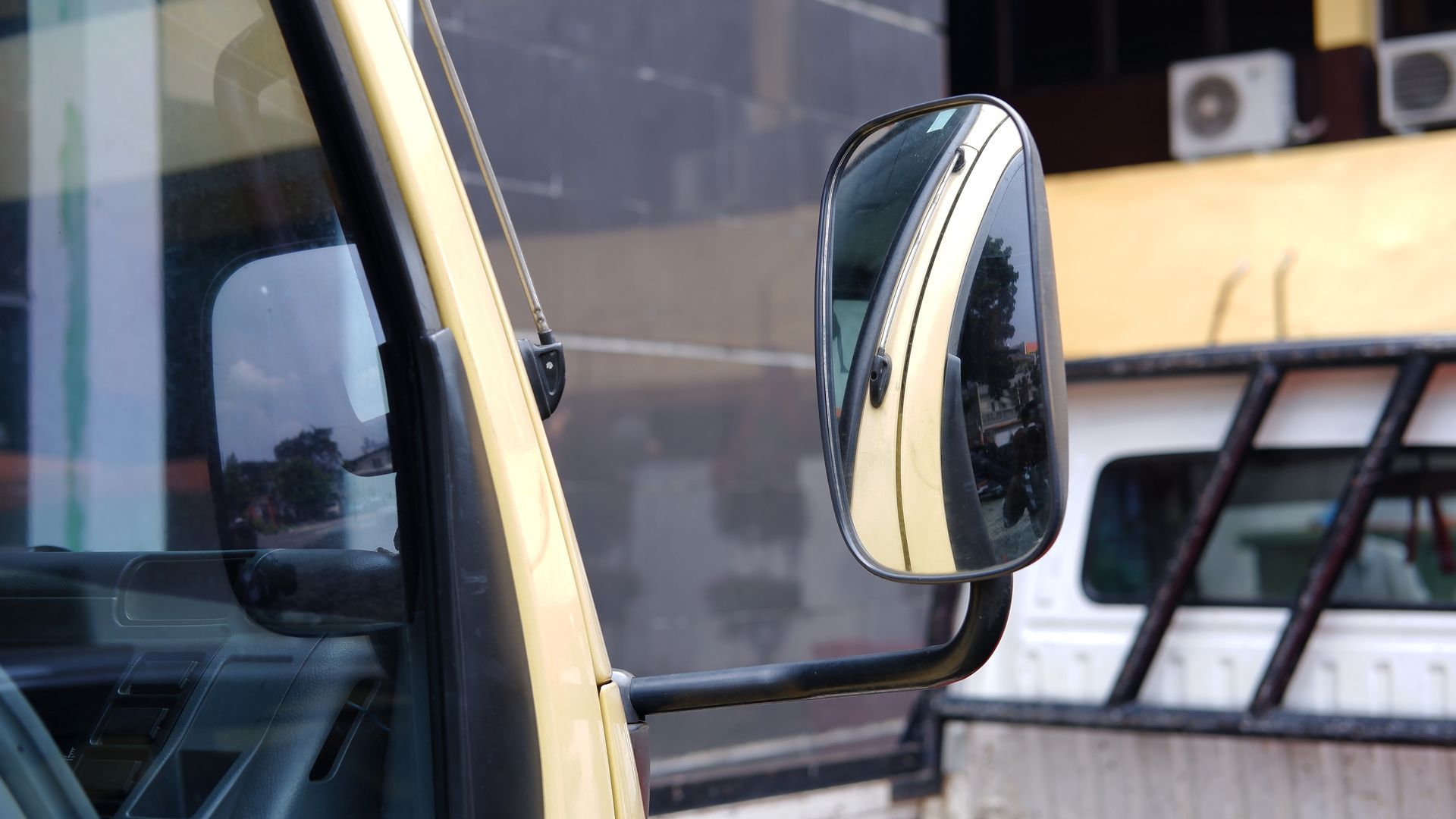 Close-up of a yellow vehicle door and side mirror beside a building window