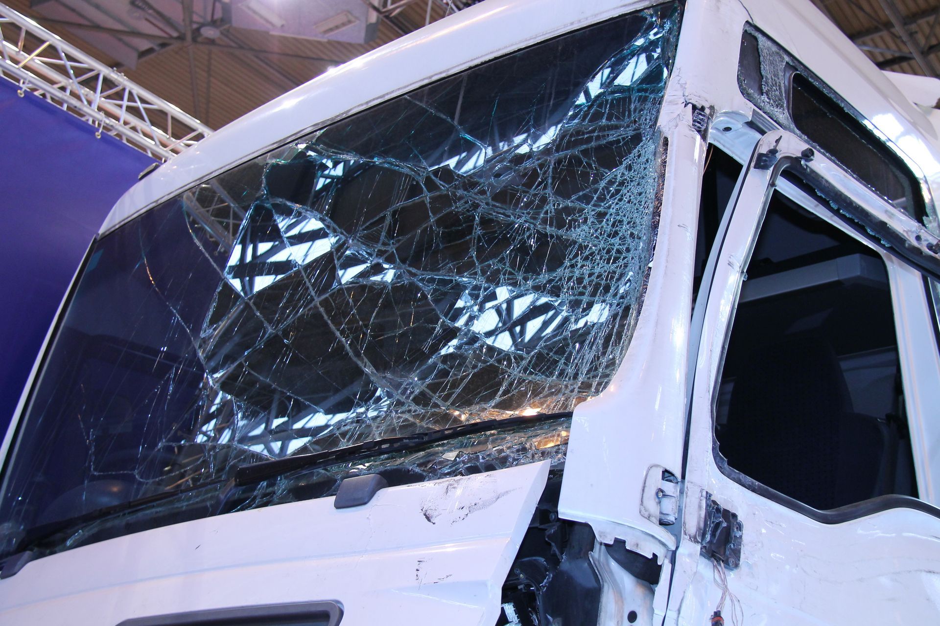 White truck cab with a shattered windshield at an indoor exhibit