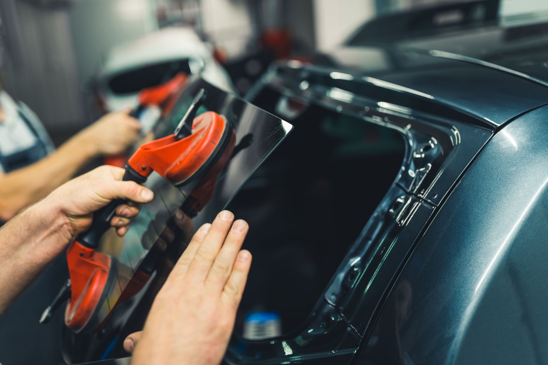 Hands using a red tool to press dark car glass, likely applying tint or film.