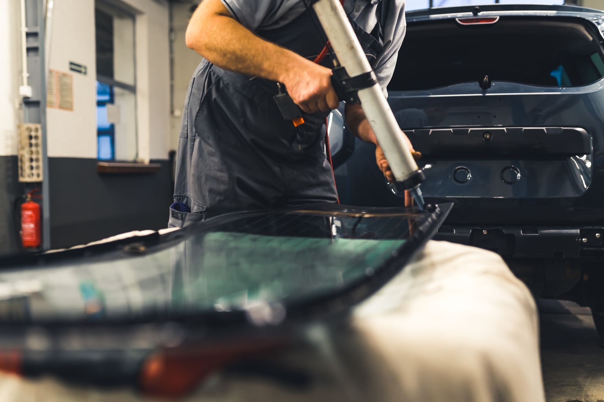 Technician using a caulking gun to seal a car windshield in an auto repair shop