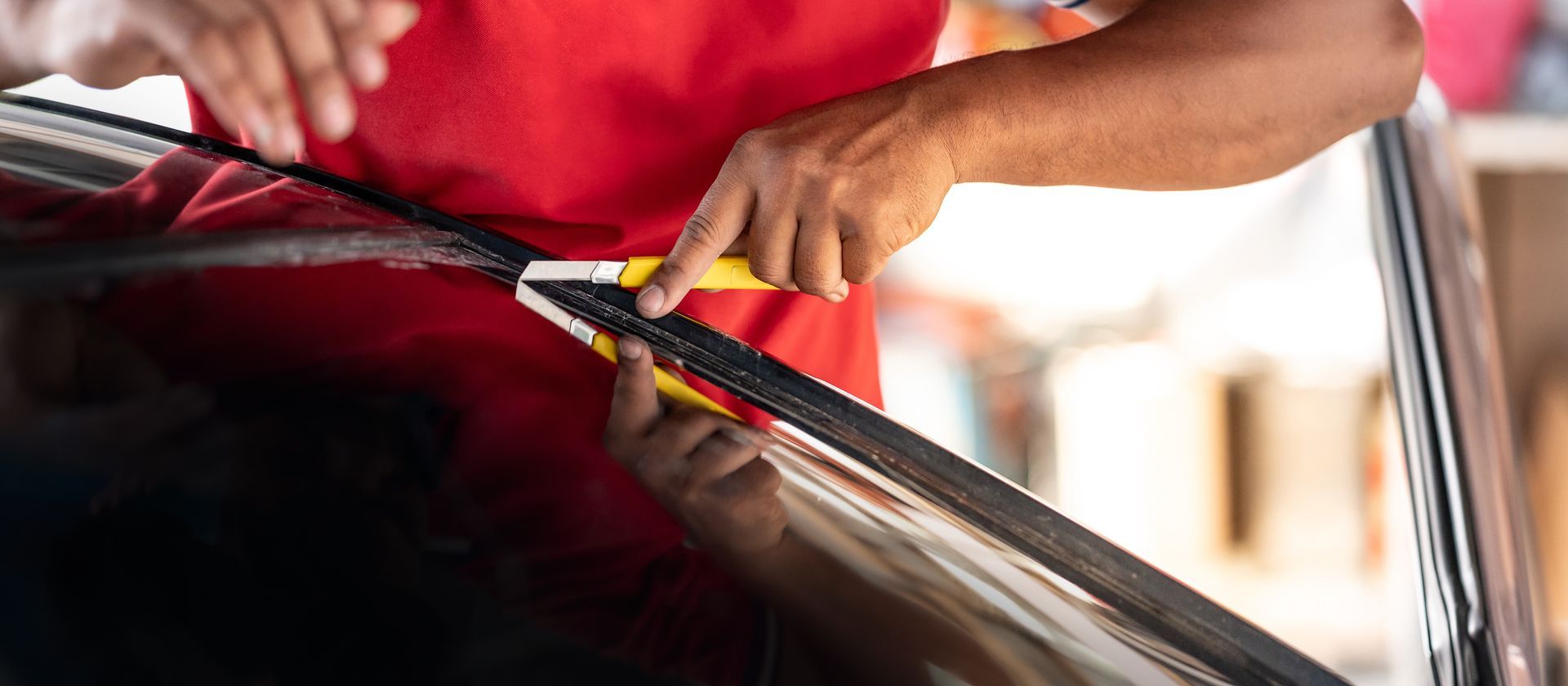 Hand using a yellow squeegee to clean a car windshield